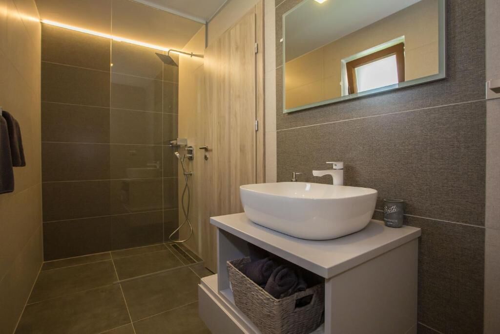 Un bagno moderno con un lavandino bianco di grandi dimensioni, uno spazio doccia in vetro e uno specchio sopra il lavandino.