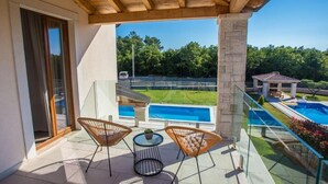 Un balcon avec deux fauteuils en osier et une petite table, donnant sur une piscine et un jardin aménagé.