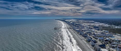 Vista aérea de uma cidade costeira com praia, cais e edifícios residenciais.
