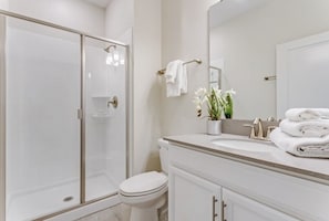 A modern bathroom with a glass shower enclosure, a white toilet, a vanity with a sink, and a mirror. - Champions Gate 4 Bedroom Townhouse by Redawning (Davenport)