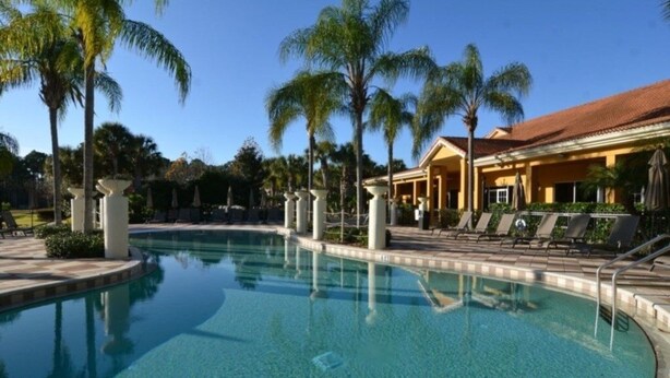 A swimming pool with lounge chairs and palm trees, surrounded by a building with a tiled roof. - 3000yl 4 Bedroom Townhouse by RedAwning (Kissimmee)