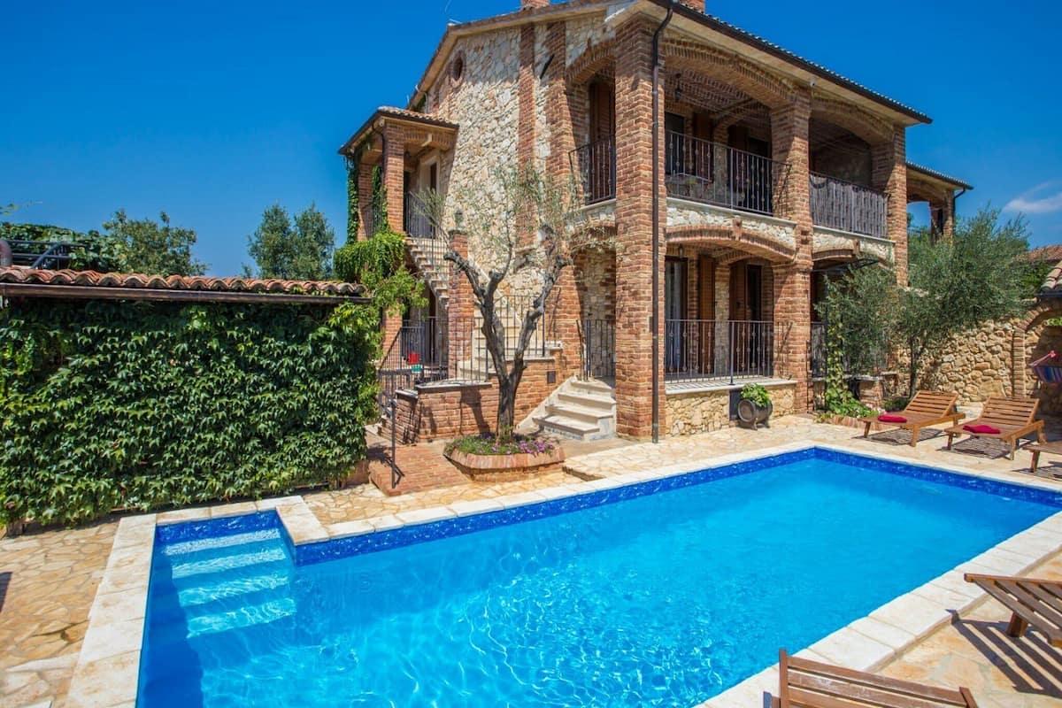 Une maison à deux étages avec une piscine, des murs en pierre et un balcon.