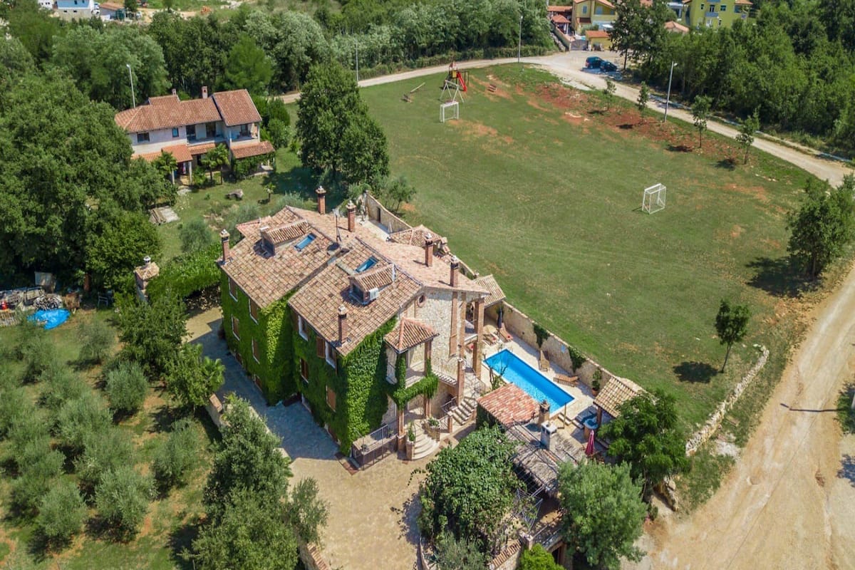 Vue aérienne d’une villa dotée d’une piscine, entourée de verdure et d’une grande pelouse.