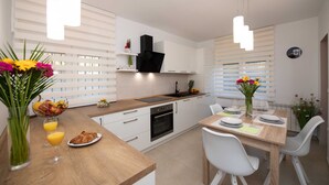 Una cocina moderna con armarios blancos, encimera de madera y un comedor con sillas blancas.