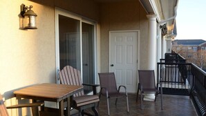 Ein Balkon mit Holztisch, zwei Stühlen, einer Tür und einem Geländer.