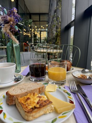 A breakfast table with a cup, a glass of red wine, a glass of orange juice, a plate with toast, cheese, and a croissant. - The People Paris Marais (Paris)