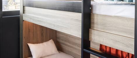 A bunk bed with a wooden headboard and a lower bed with a white mattress and a single pillow.