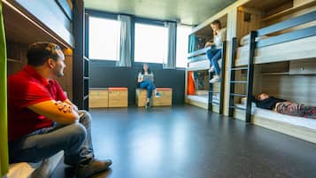 Een slaapzaal met stapelbedden, een houten vloer en een raam met gordijnen.