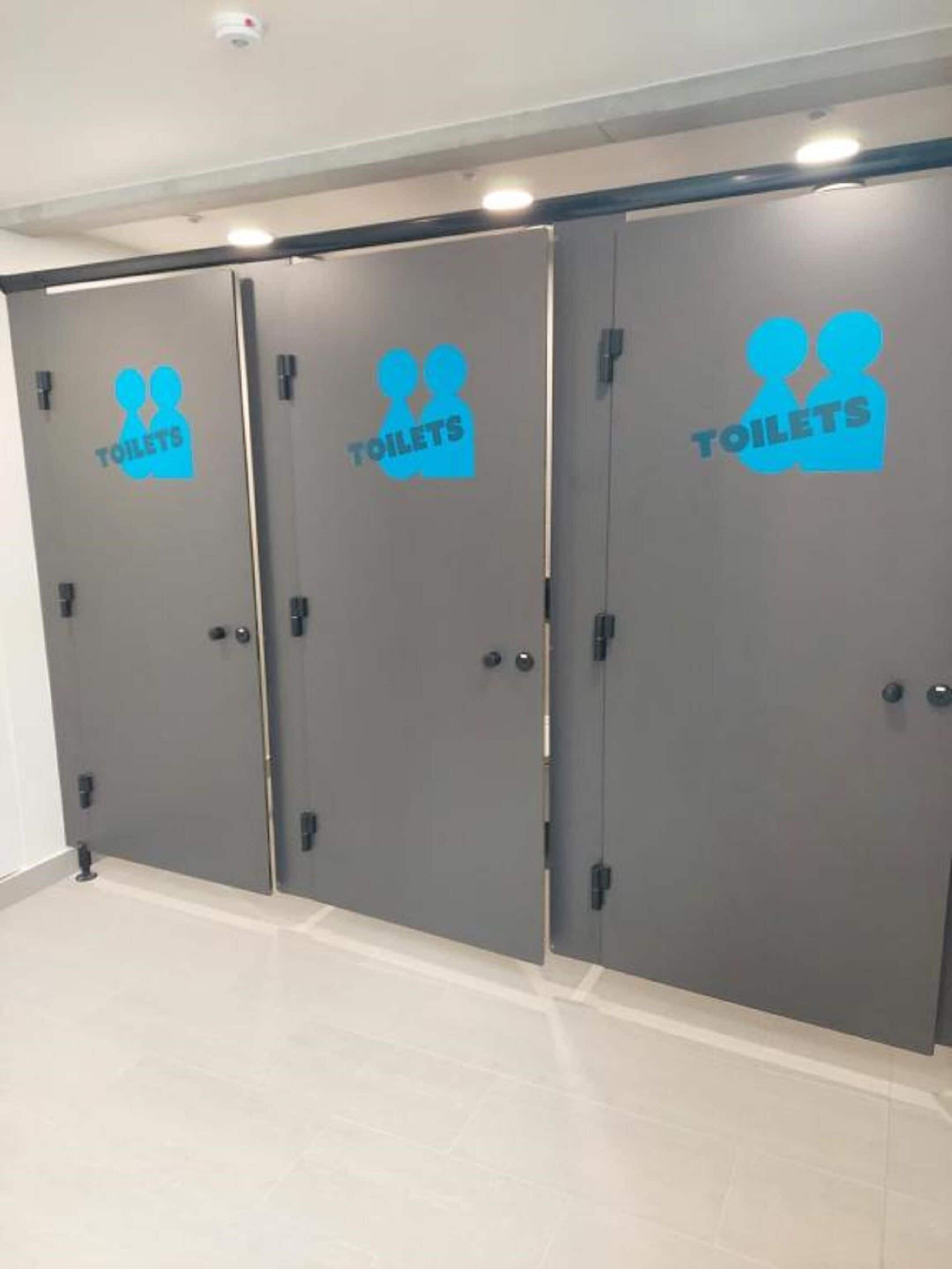 Three grey doors with blue icons and the word "TOILETS" on them, indicating a restroom area.
