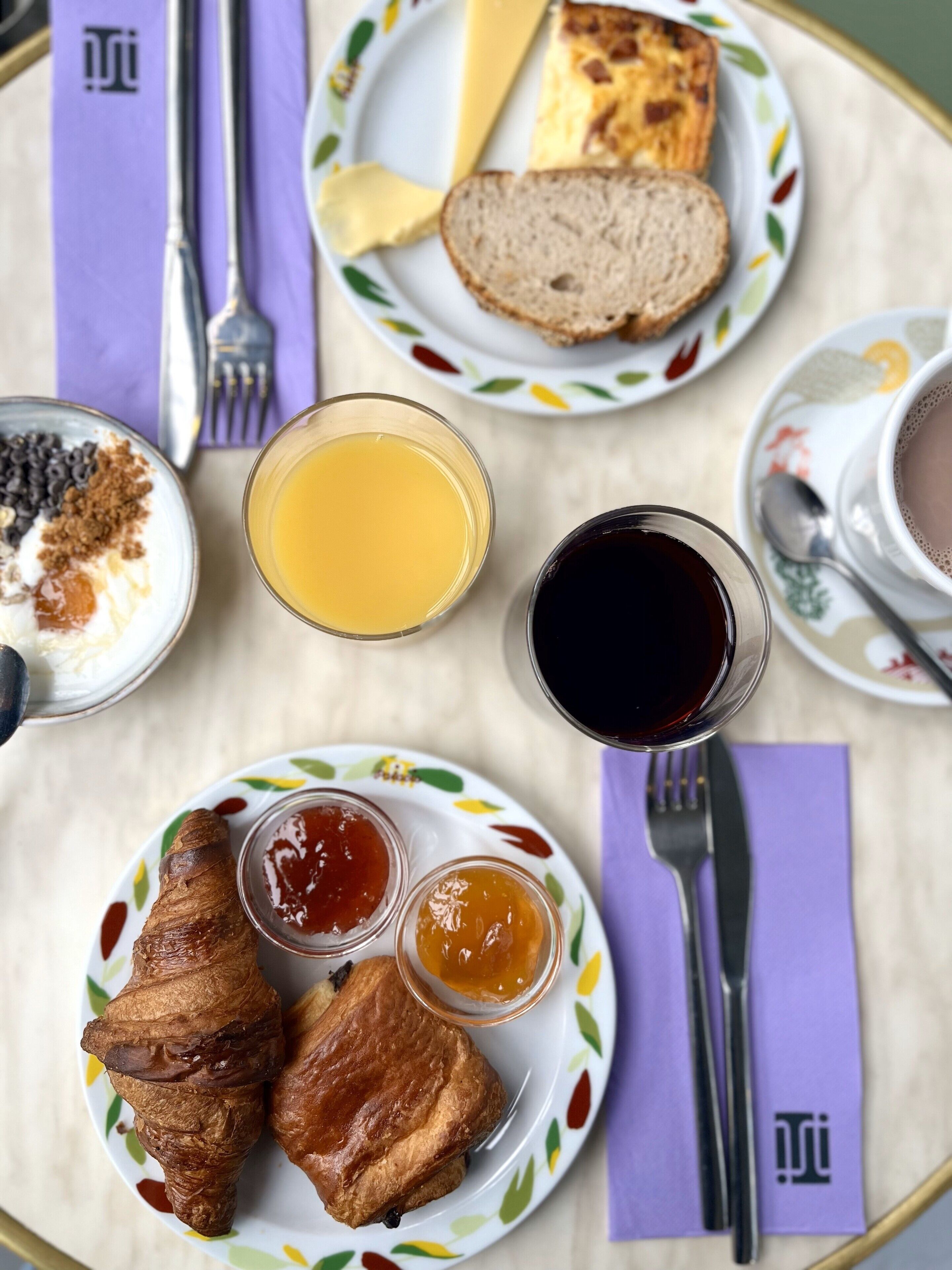 Una colazione con croissant, pane, marmellata e un bicchiere di succo d'arancia su un tavolo.