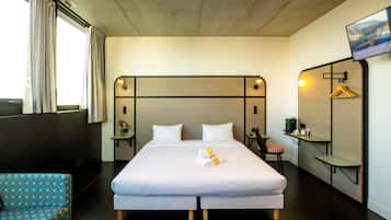 A hotel room with a bed, a chair, a TV, and a small table with a coffee machine.