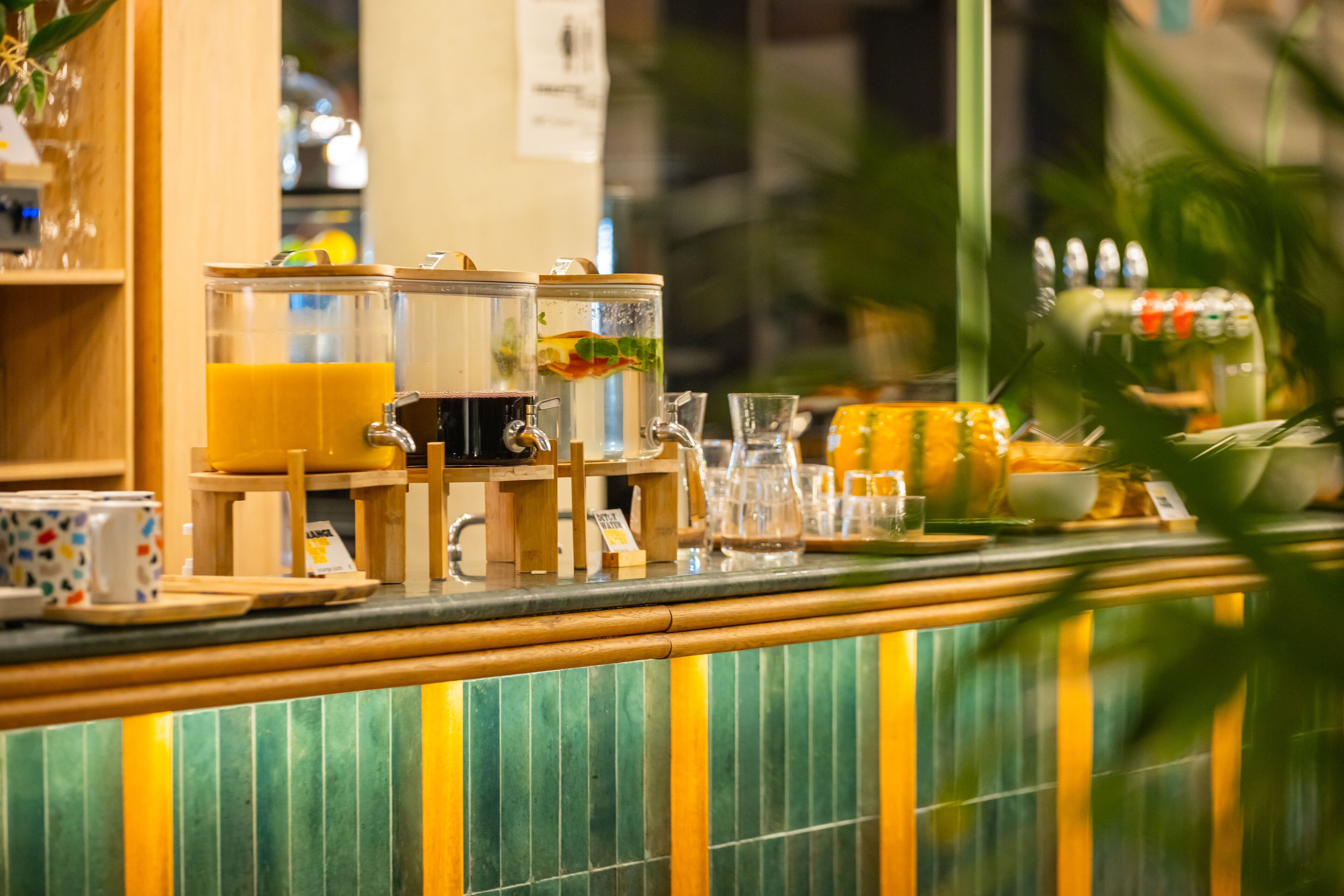 Un espace bar avec un comptoir, divers récipients en verre et un mur recouvert de carreaux verts.