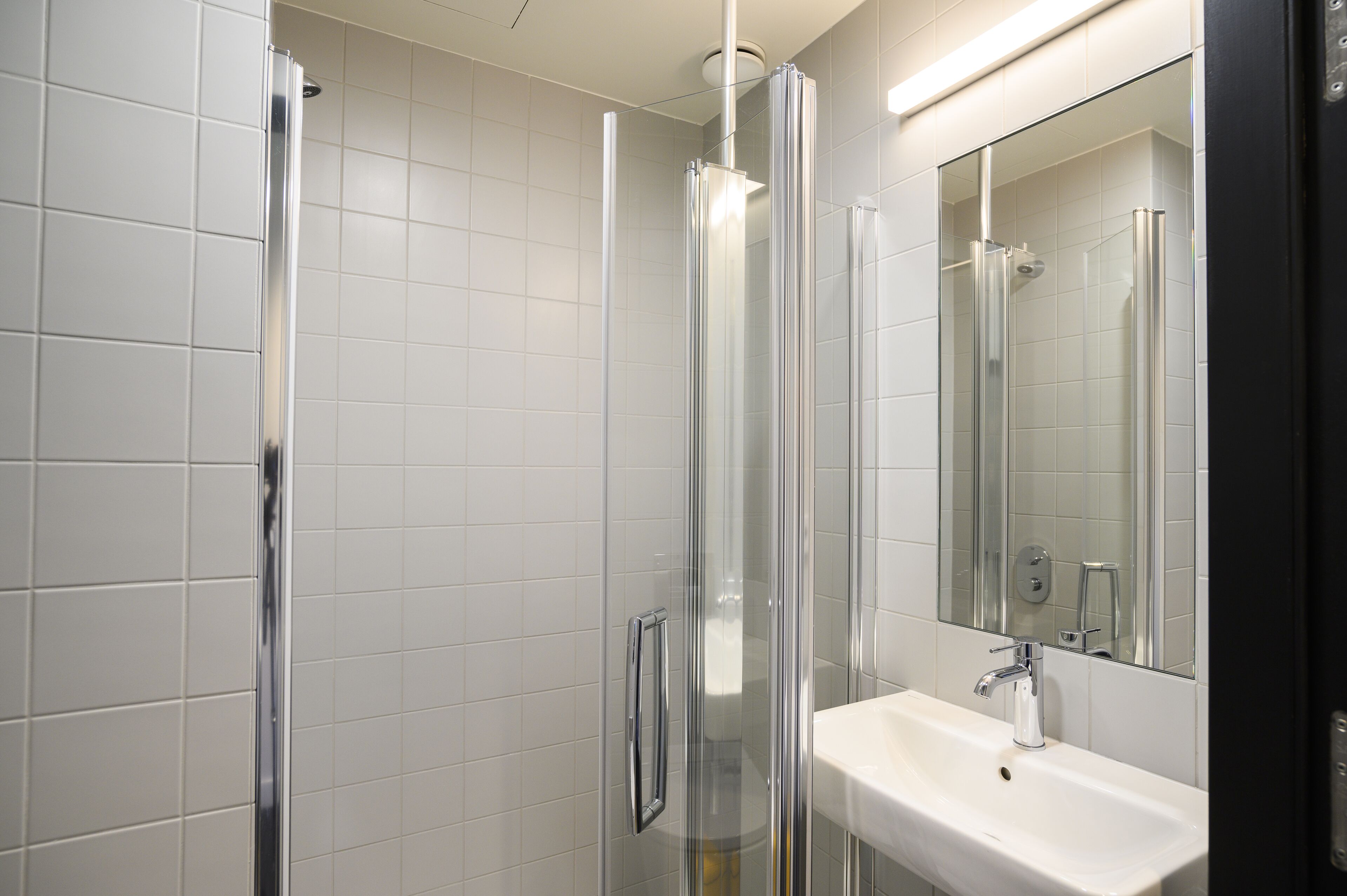 A modern bathroom with a glass shower enclosure, a white sink, and a large mirror.