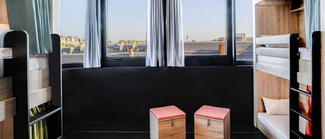 A compact train compartment with a bunk bed, a small seating area, and a window offering a city view.