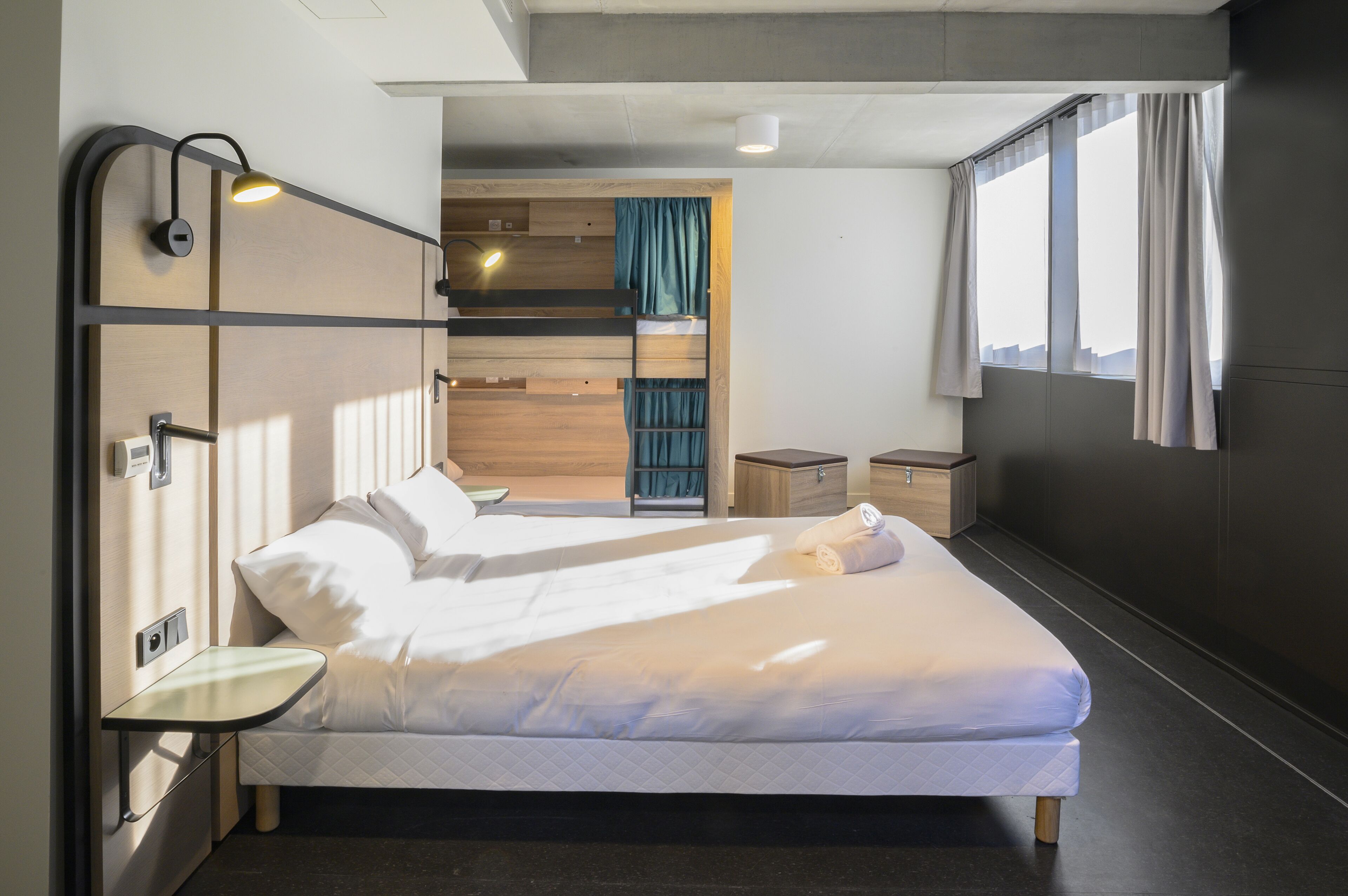 A modern hotel room with a large bed, bedside tables, a wardrobe, and a window with curtains.