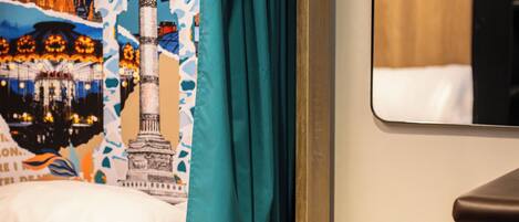 A bed with a teal curtain, a wooden headboard, and a wall with a Paris-themed poster.