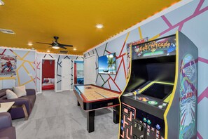 Una stanza con tavolo da biliardo, divano, ventola a soffitto e una macchina arcade.