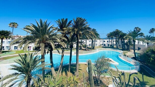 Un resort con una gran piscina rodeada de palmeras y un cielo azul despejado.