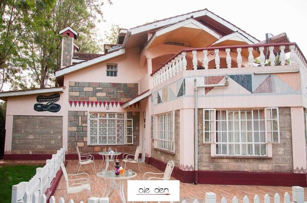 Una casa a due piani con un balcone, una facciata in pietra e un piccolo portico con sedie e tavoli.