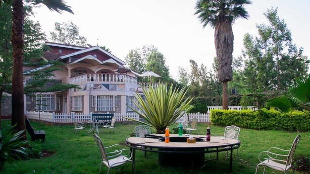 Un giardino con un tavolo rotondo e sedie, una palma e un edificio sullo sfondo con una recinzione bianca.