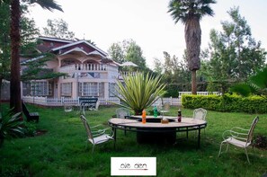 Un giardino con un tavolo rotondo e sedie, una palma e un edificio sullo sfondo con una recinzione bianca.
