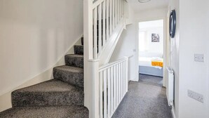 Eine Treppe mit weißen Geländern führt zu einem Raum mit einem Bett und einem Heizkörper.