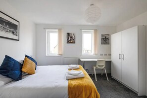 A hotel room with a bed, two windows, a desk, and a wardrobe.