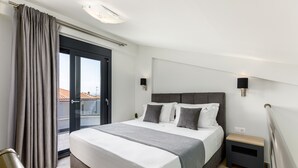 Habitación de hotel moderna con una cama grande, una mesita de noche pequeña y vistas a la ciudad a través de un ventanal amplio.