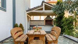 Un patio con mesa y bancos de madera, piso de piedra y horno de ladrillo.