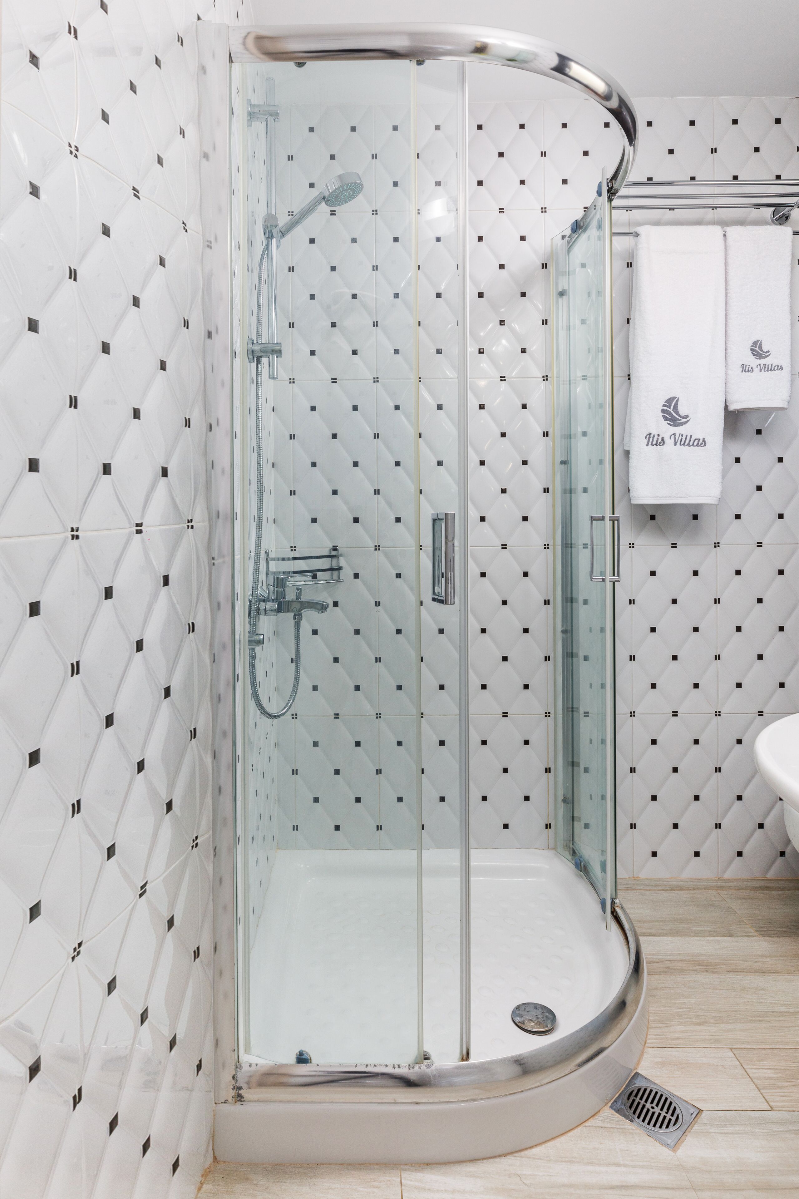 Un baño moderno con cabina de ducha de vidrio, paredes con azulejos blancos y un lavamanos blanco.