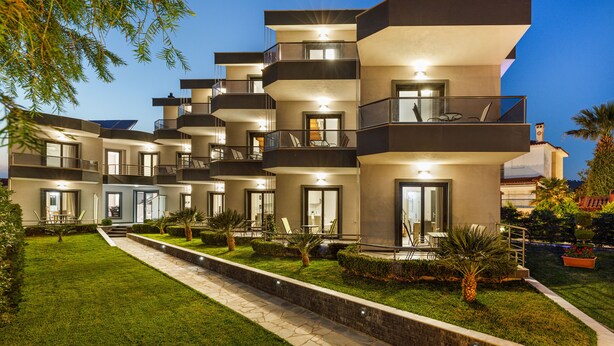 Un edificio residencial moderno de varios pisos con balcones, un césped cuidado y un camino de piedra.