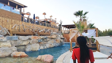 Una terraza de madera con piscina, rodeada de rocas y palmeras.