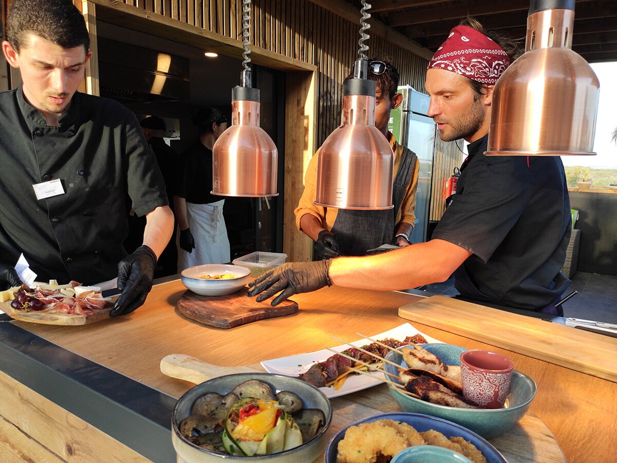 A chef preparing food at a counter with copper kitchen lights, a bowl of vegetables, and a plate of meat.