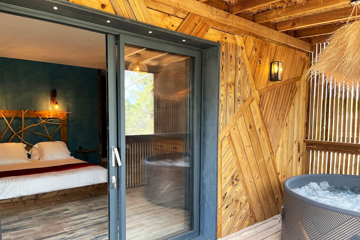 Une chambre avec une porte-fenêtre coulissante donnant sur un balcon, un plafond en bois et un jacuzzi.
