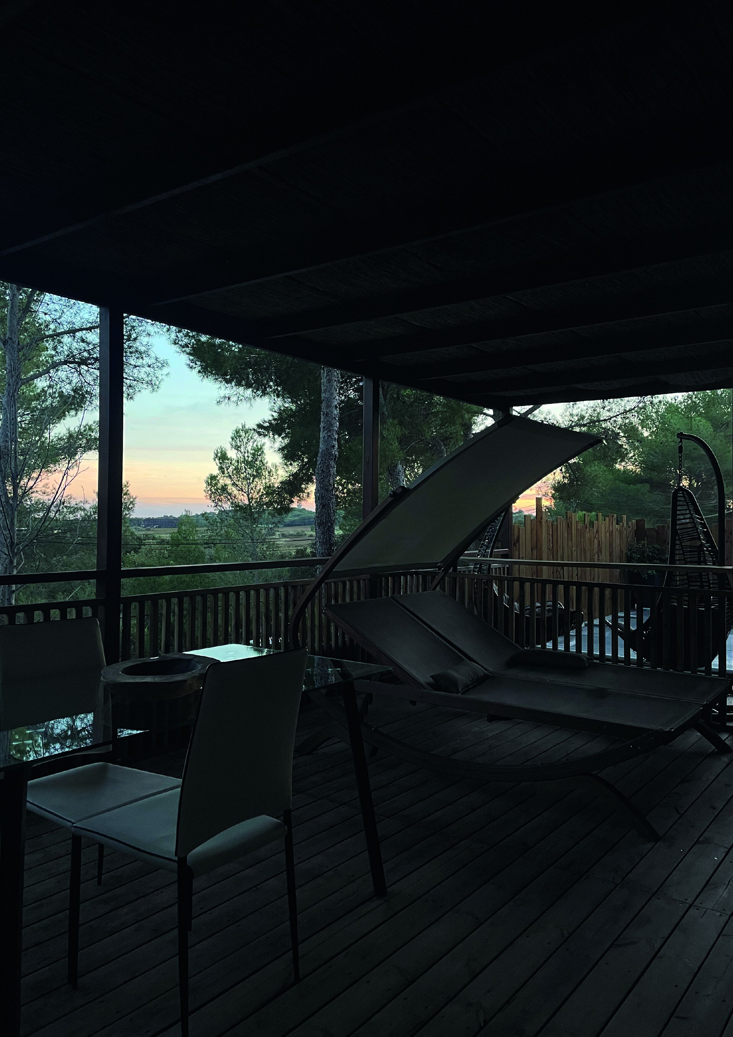 A covered outdoor area with a wooden deck, a swing chair, and a lounge chair.