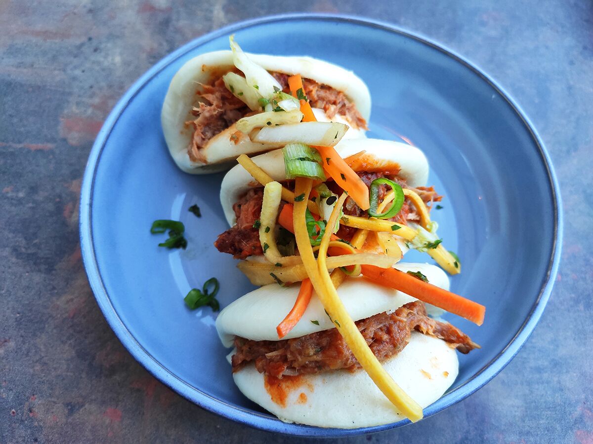A plate of bao buns with shredded meat and vegetables.