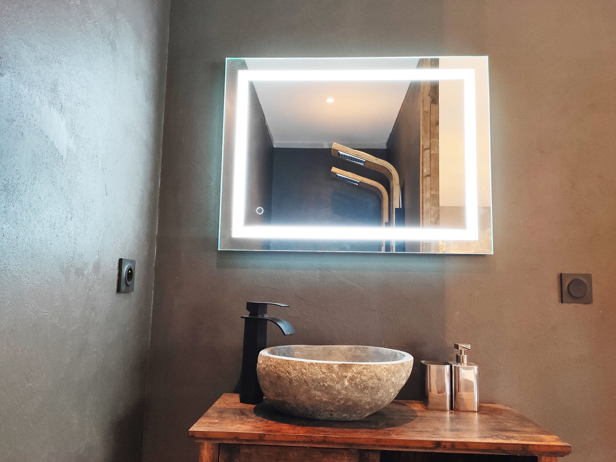 A bathroom with a stone sink, a modern faucet, and a rectangular mirror with LED lighting.