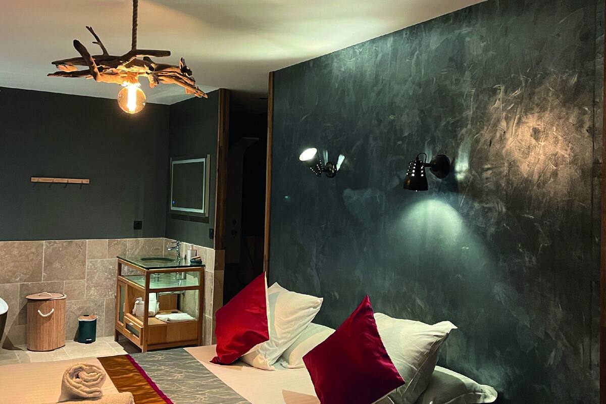 Une chambre d’hôtel moderne dotée d’un grand lit, d’une tête de lit en bois, d’une coiffeuse au plateau en verre et d’un luminaire au plafond au design original.