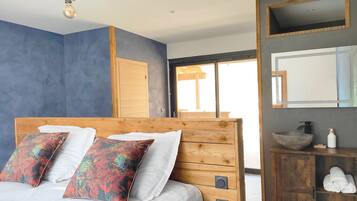 A bedroom with a wooden headboard, a large bed with white linens, two decorative pillows, a wooden nightstand with a bowl and toiletries, and a large mirror above the nightstand.