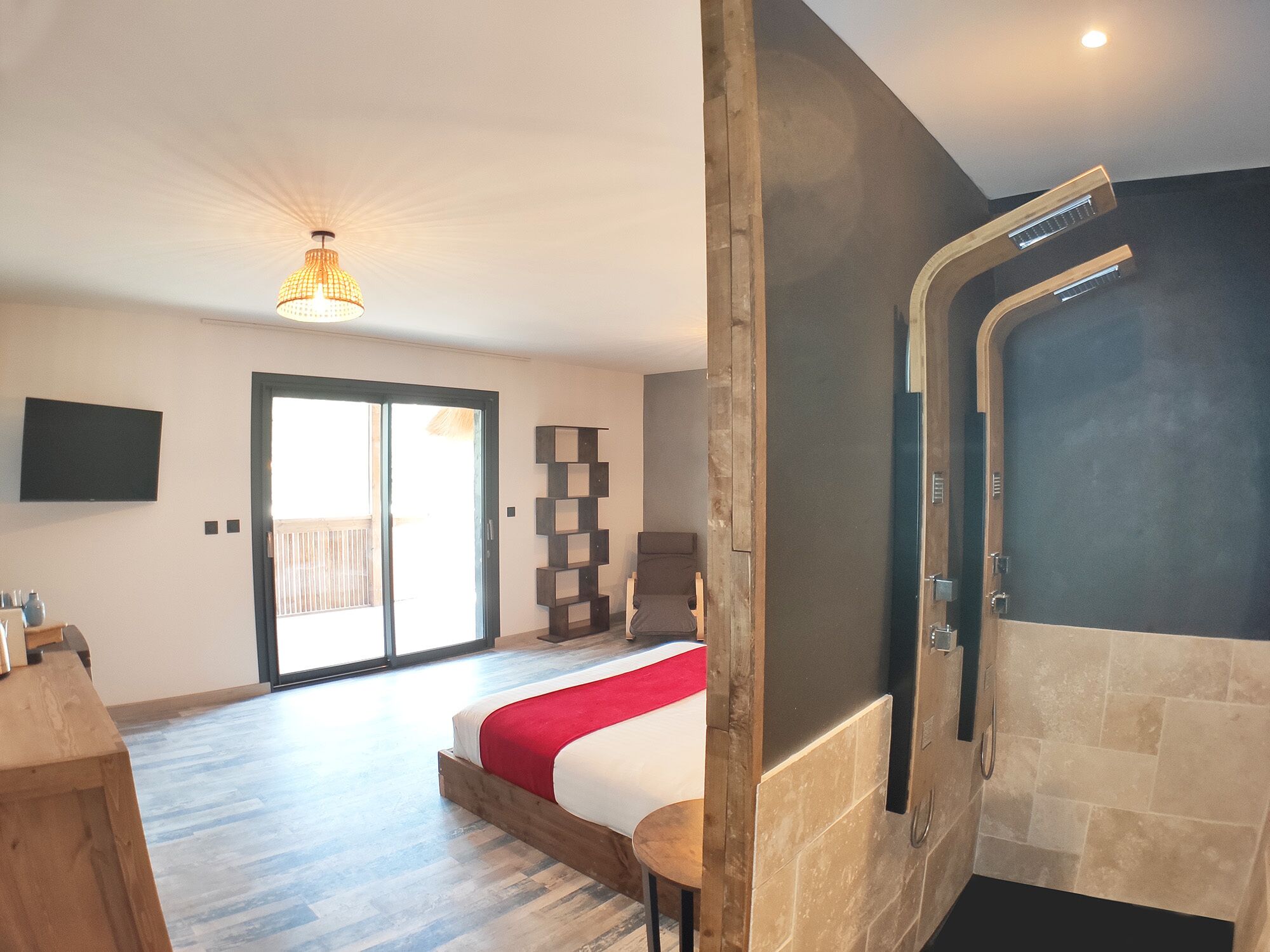 A modern hotel room with a large bed, a wooden bench, a wall-mounted TV, and a sliding door leading to a balcony.
