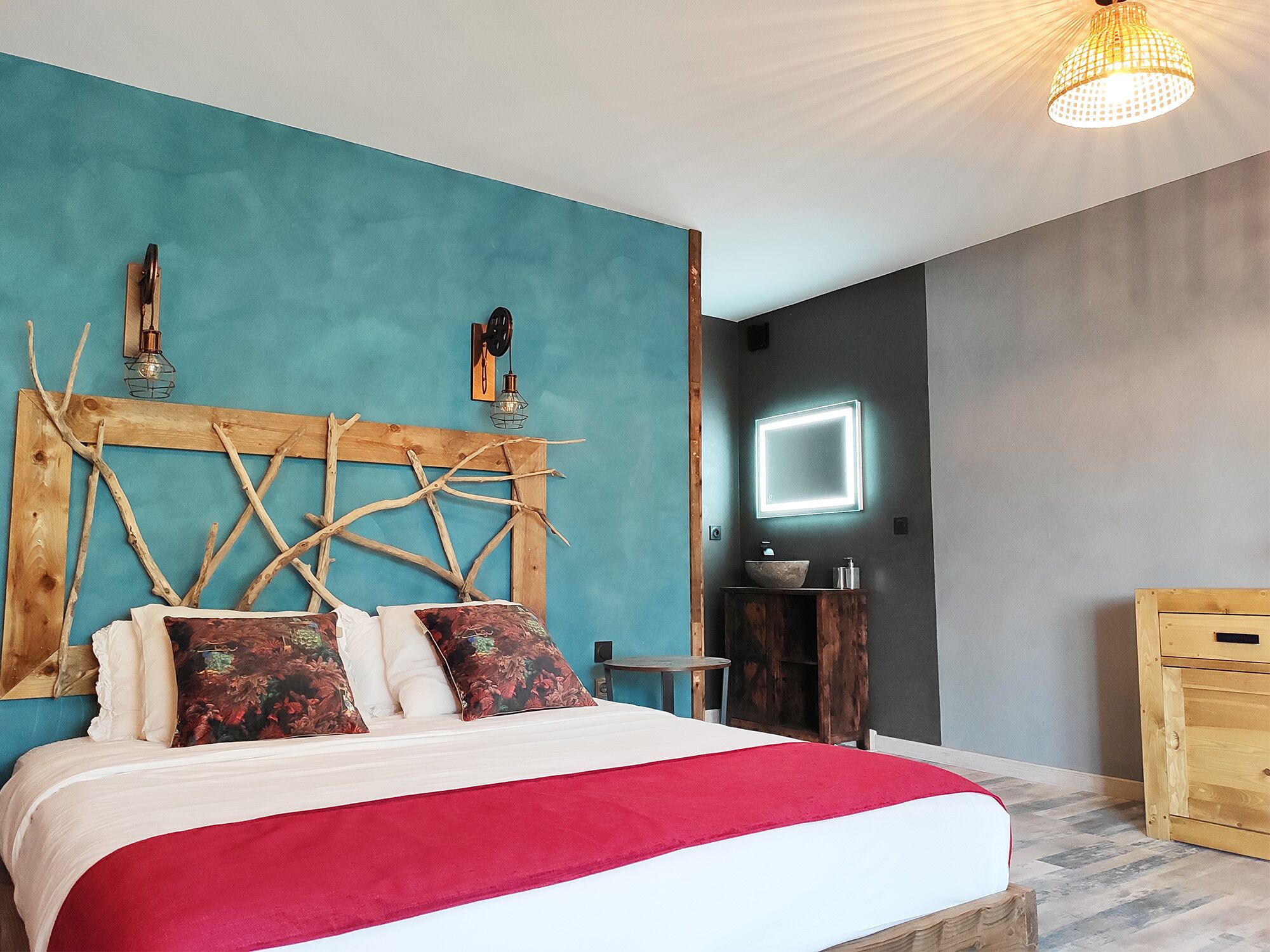 A bedroom with a bed, a wooden headboard, a bedside table, a nightstand, a mirror, and a dresser.