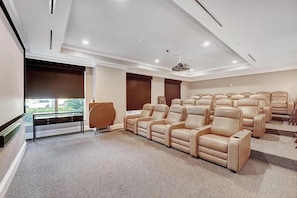 Ein Heimkino mit bequemen, beigefarbenen Liegesesseln, einer großen Leinwand und einem Teppichboden.