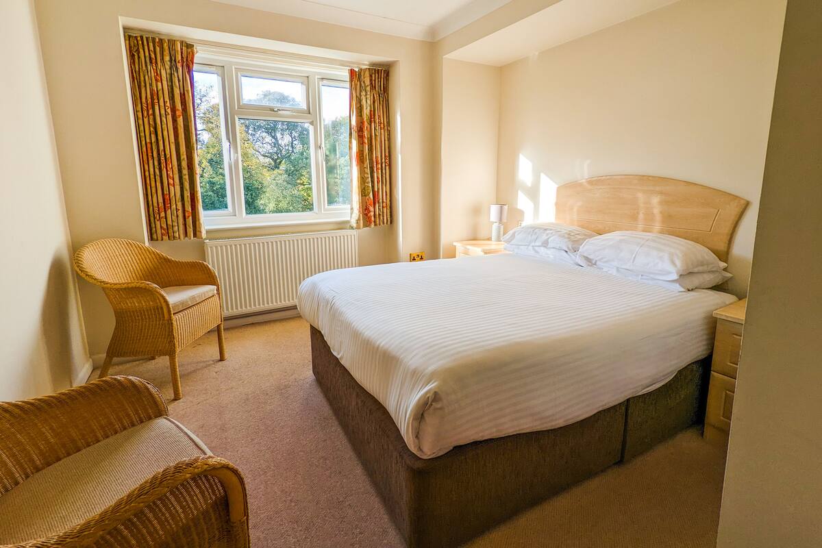 A hotel room with a large bed, a chair, a nightstand, and a window with curtains.