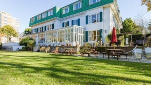 A two-story building with a green roof and white walls, featuring a glass conservatory and outdoor seating area with tables and chairs. - THE GROVE HOTEL (Bournemouth)