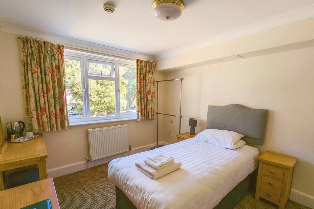 A bedroom with a bed, bedside tables, a desk, a radiator, and a window with curtains.