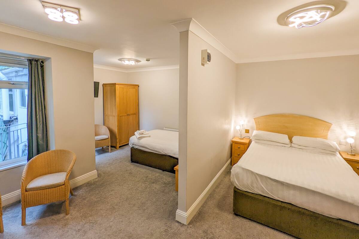 A hotel room with a bed, a chair, a wardrobe, and a window with curtains.