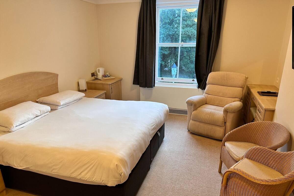 A hotel room with a large bed, a chair, a desk, and a window with curtains.