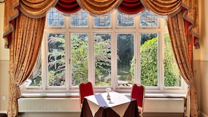 A room with a large window, red curtains, and a table with chairs. - THE GROVE HOTEL (Bournemouth)