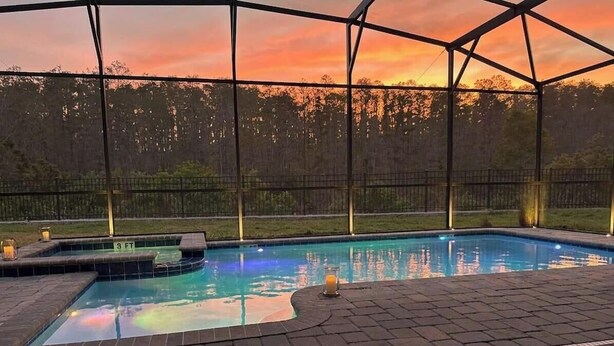 A swimming pool with a view of trees and a sunset.