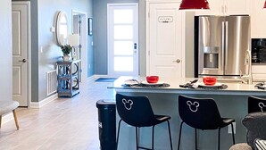 A modern kitchen with a stainless steel refrigerator, a red pendant light, and a bar area with black chairs.